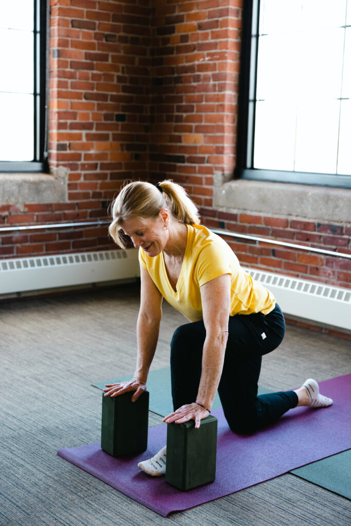 Movement and Fitness instructor, Tish, is demonstrating a kneeling yoga pose using yoga blocks. 